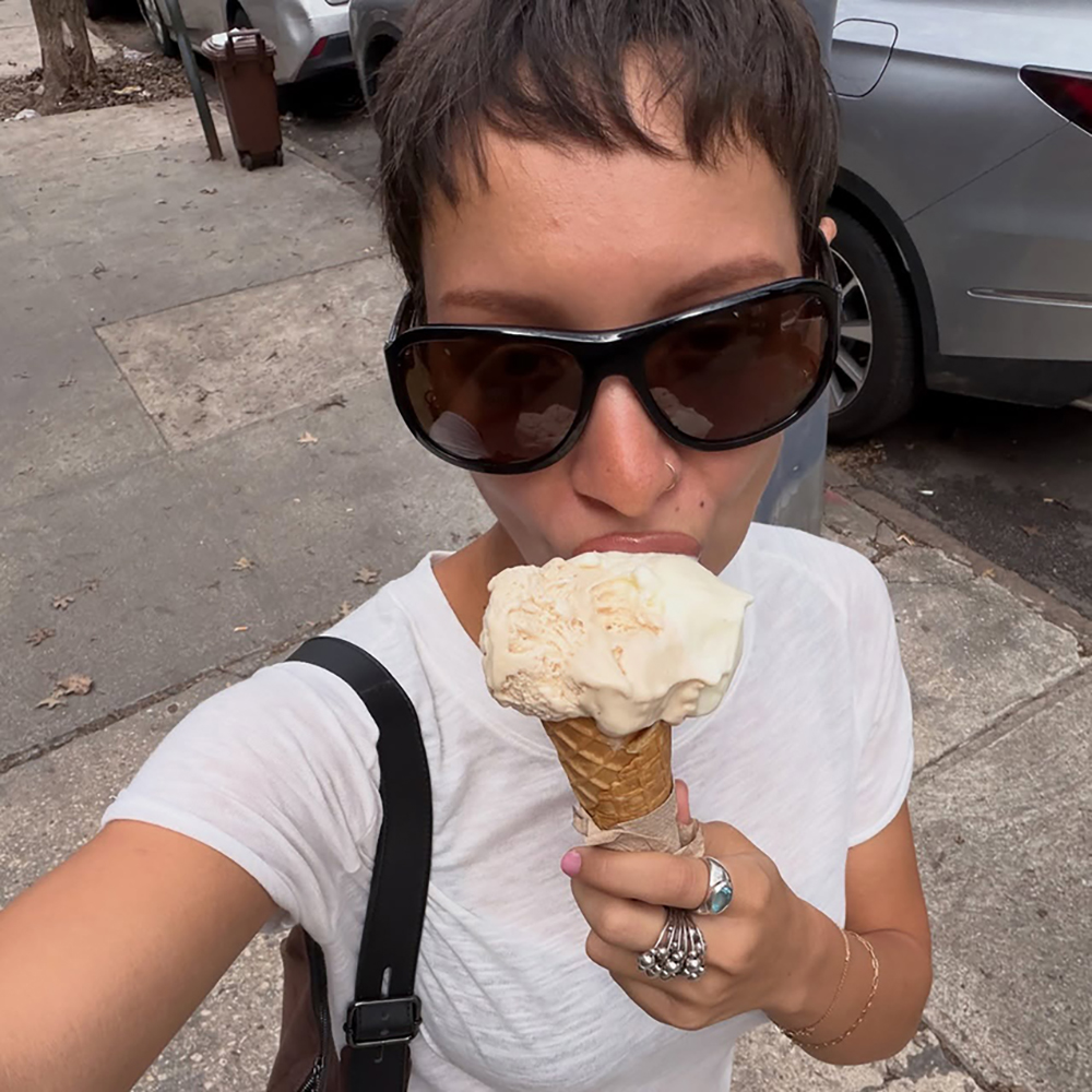 a woman wearing brown sunglasses, white tee, yellow skirt, brown suede bag