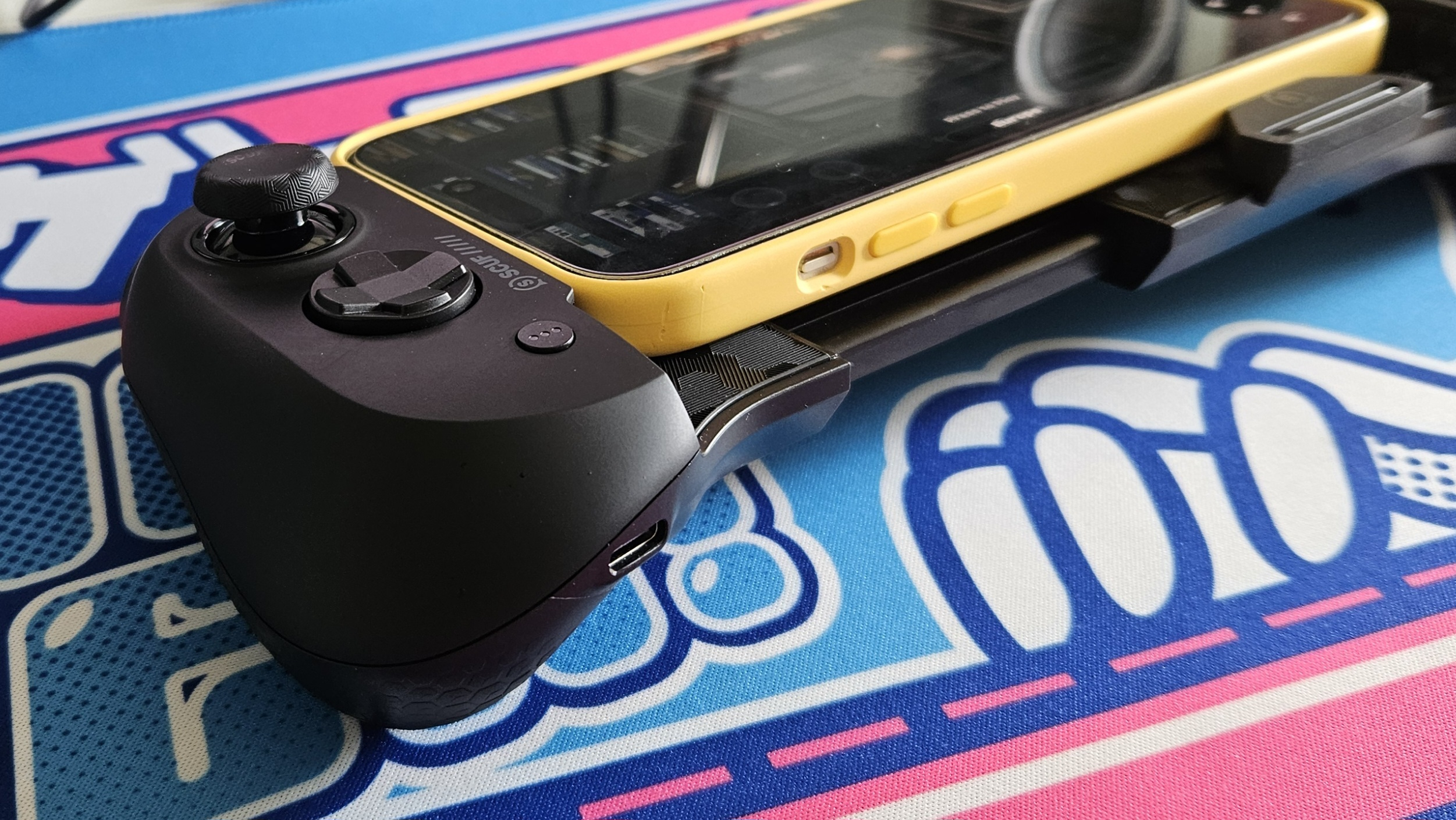 The Scuf Nomad and a mobile phone on a colorful desk mat.