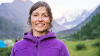 A smiling woman in the mountains wearing a purple fleece