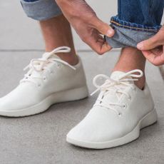 A pair of white Allbirds shoes with someone folding up jeans 