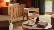 Lulu and Georgia fall 2025 home collection, including low slung boucle accent chairs, a pink marble coffee table, moss green rug, geometrically etched wooden sideboard, and sculpural accents, pictured in a sunlit living room