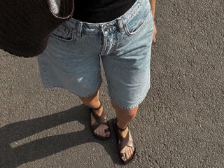 Woman wears A. Emery Jalen leather sandals, Arket long shorts, a black Loewe tank top and a Dragon Diffusion bag while walking.