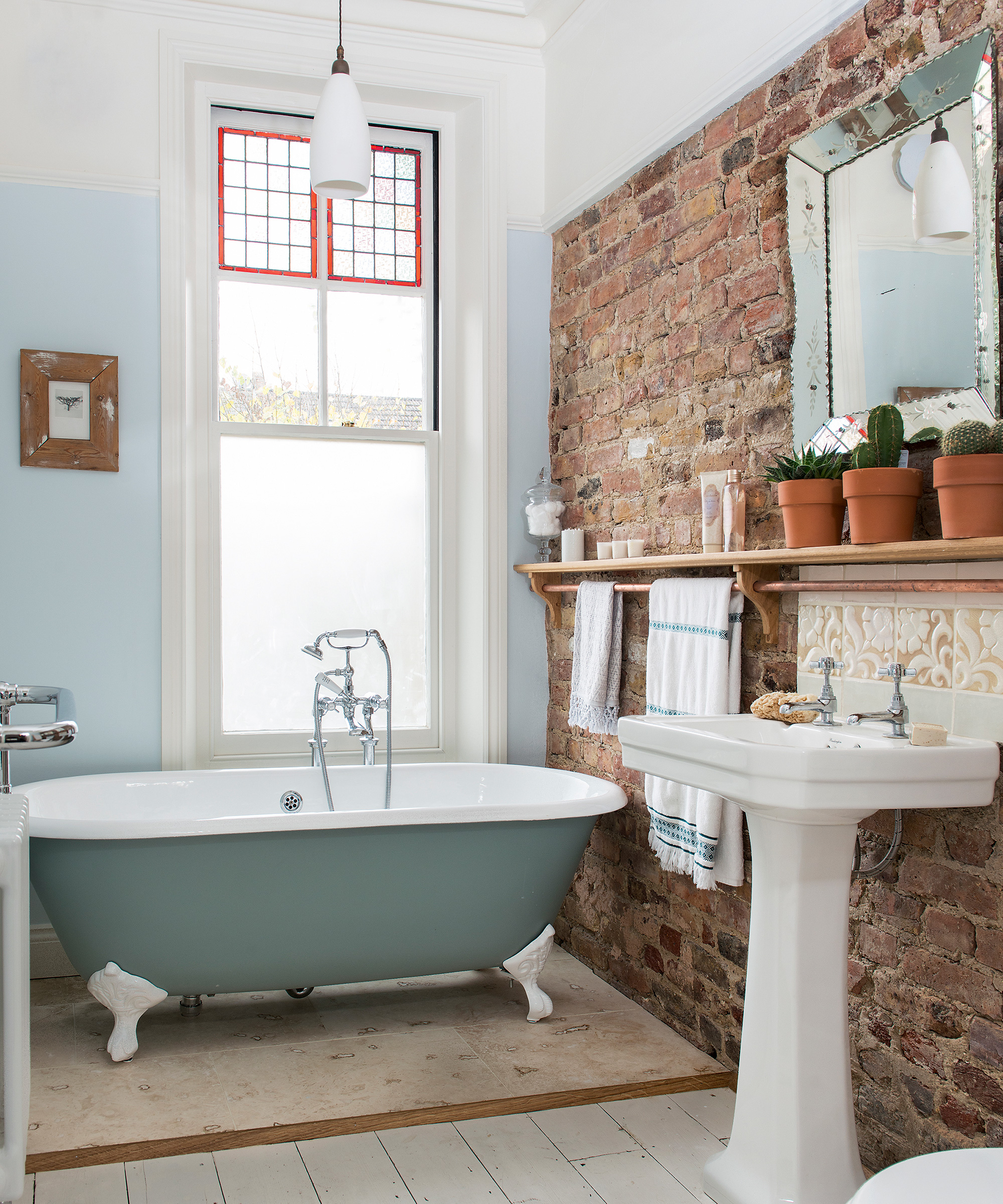 A small bathroom with an exposed brick wall and roll top bath