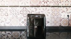 A black air fryer in kitchen with retro brown and white patterned wall tile decor