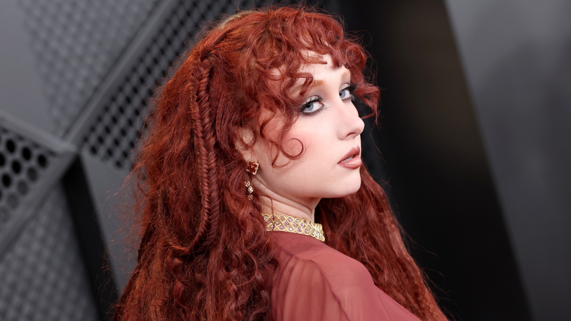 a white woman with curly red hair poses on a red carpet before an awards show