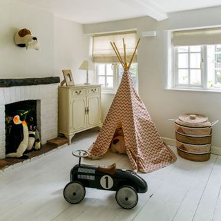 Childrens play room with beige chest of drawers, kids play tent, toy racing car, stuffed penguins and fire place