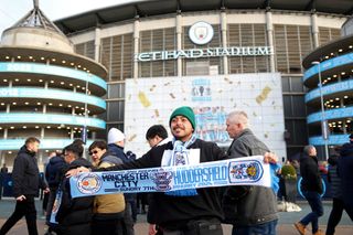 A fan poses for a photo with a half and half scarf outside the stadium prior to the Emirates FA Cup Third Round match between Manchester City and Huddersfield Town at Etihad Stadium on January 07, 2024 in Manchester, England