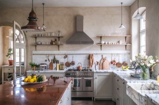 Our Food Stories kitchen with plaster colored walls, marble countertops, copper top island, open shelving, flowers, hanging rail