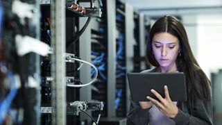 A woman looking at a tablet while standing in front of a server rack