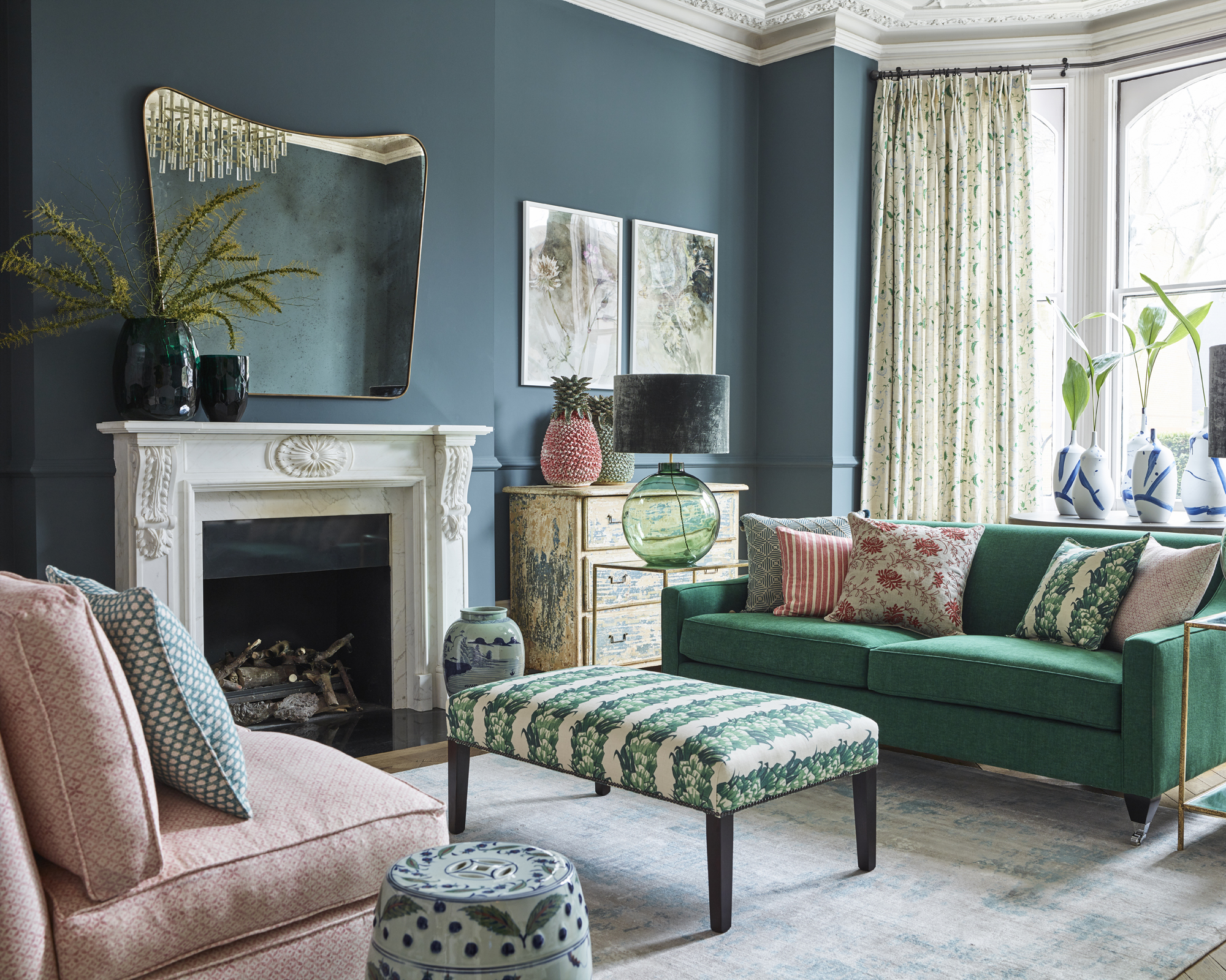 A living room mirror idea with green-blue walls and a bowed shaped mirror above fireplace