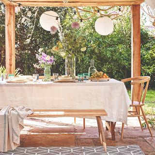 A garden with a set wooden garden dining set under a gazebo with lanterns