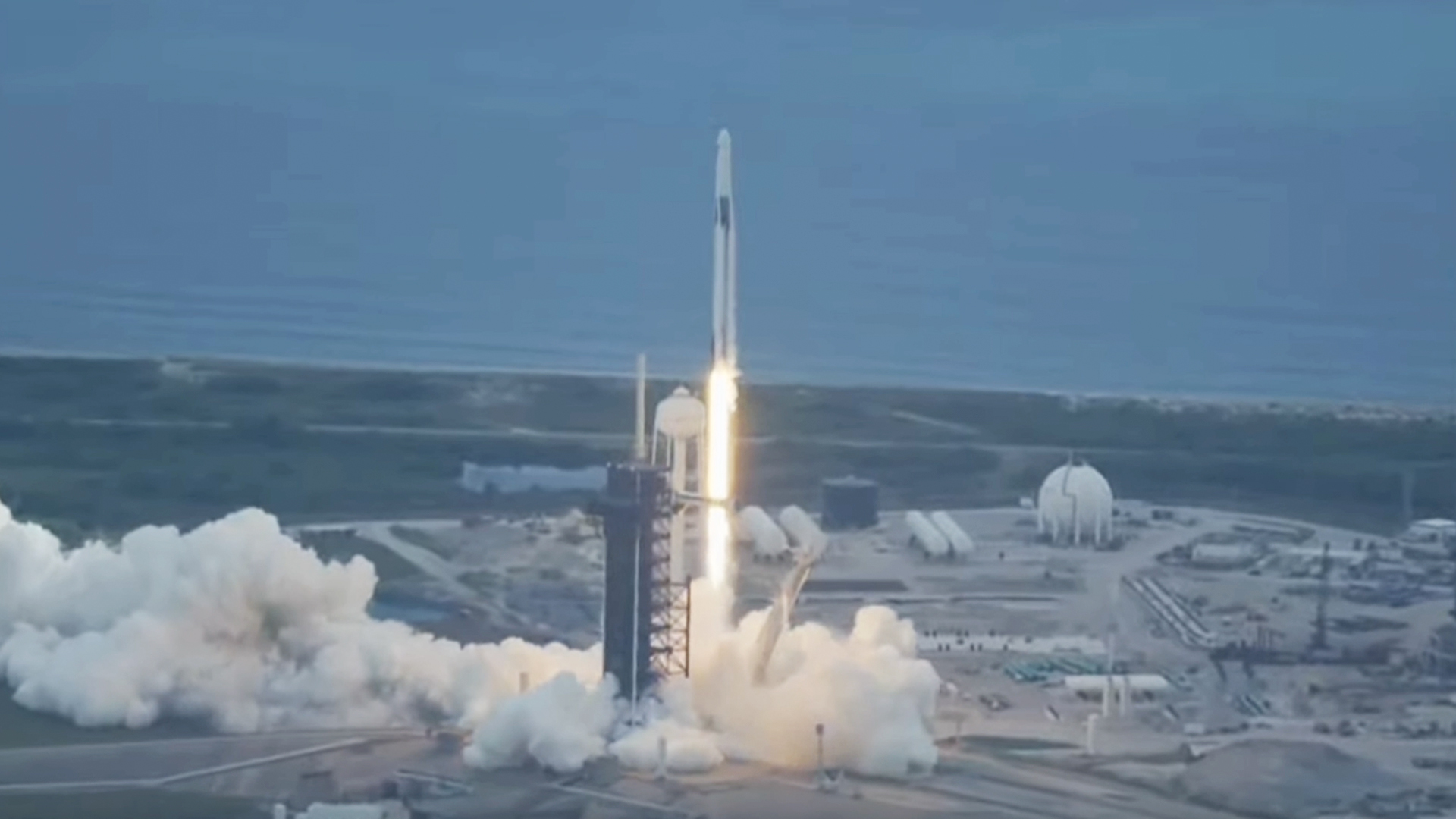 A rocket seen shooting upward with a coastline in the background.
