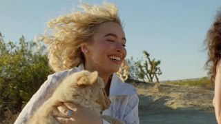 Sabrina Carpenter pants-free and holding a dog while her hair blows in the wind in the Manchild music video.