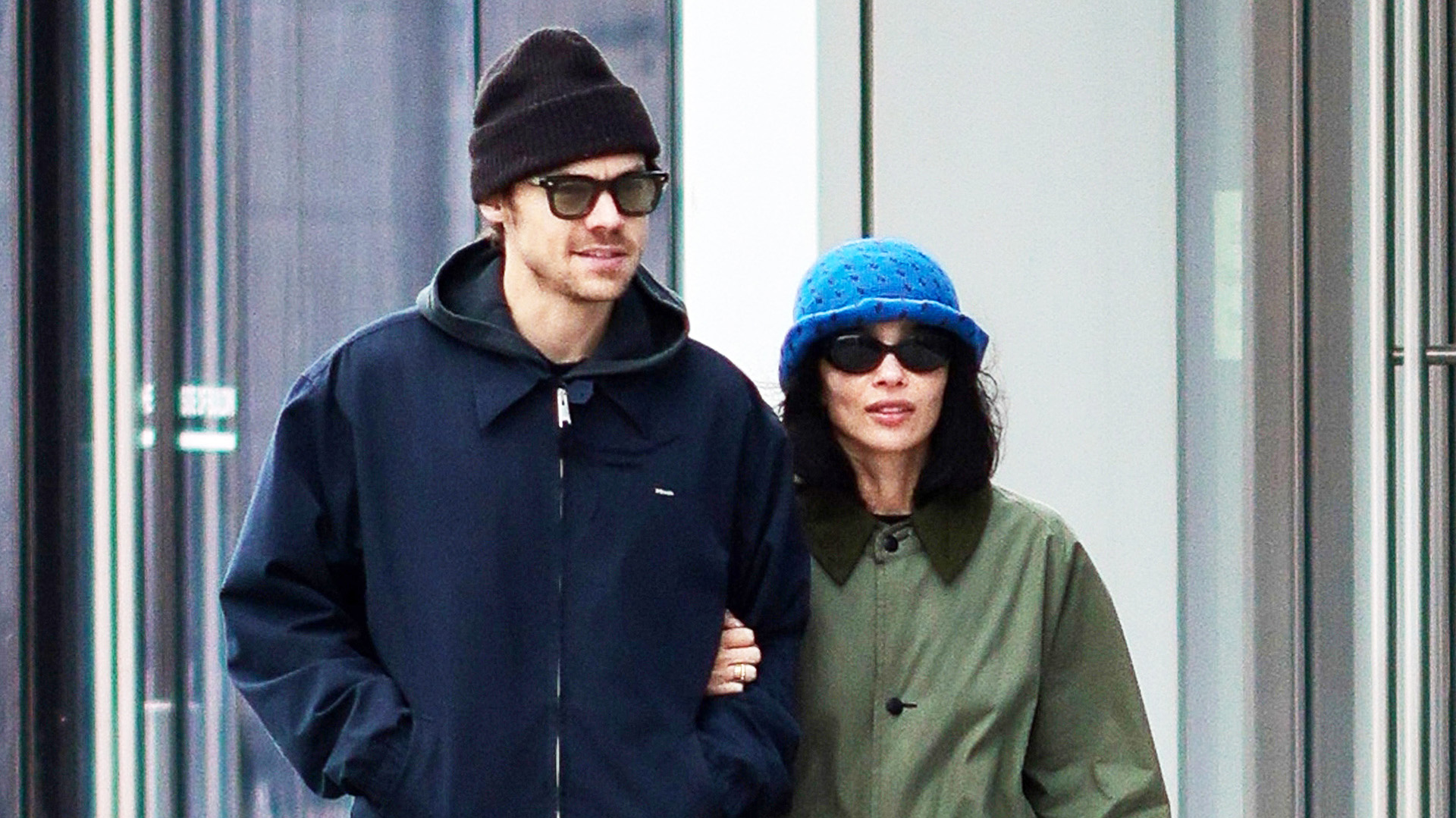 Zo&euml; Kravitz walking with Harry Styles in NYC while wearing an olive green coat, black pants, black sneakers, a The Row Ingrid bag, and blue crochet bucket hat