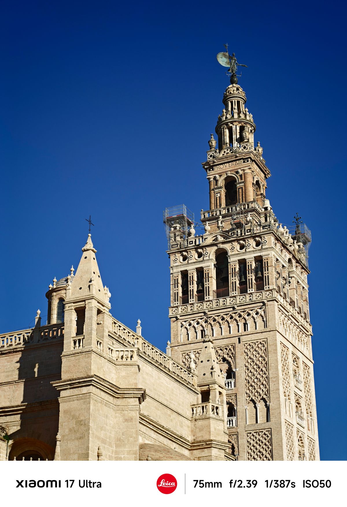 Close-up of the Giralda bell tower&rsquo;s ornate upper section topped with the El Giraldillo statue against a deep blue sky.