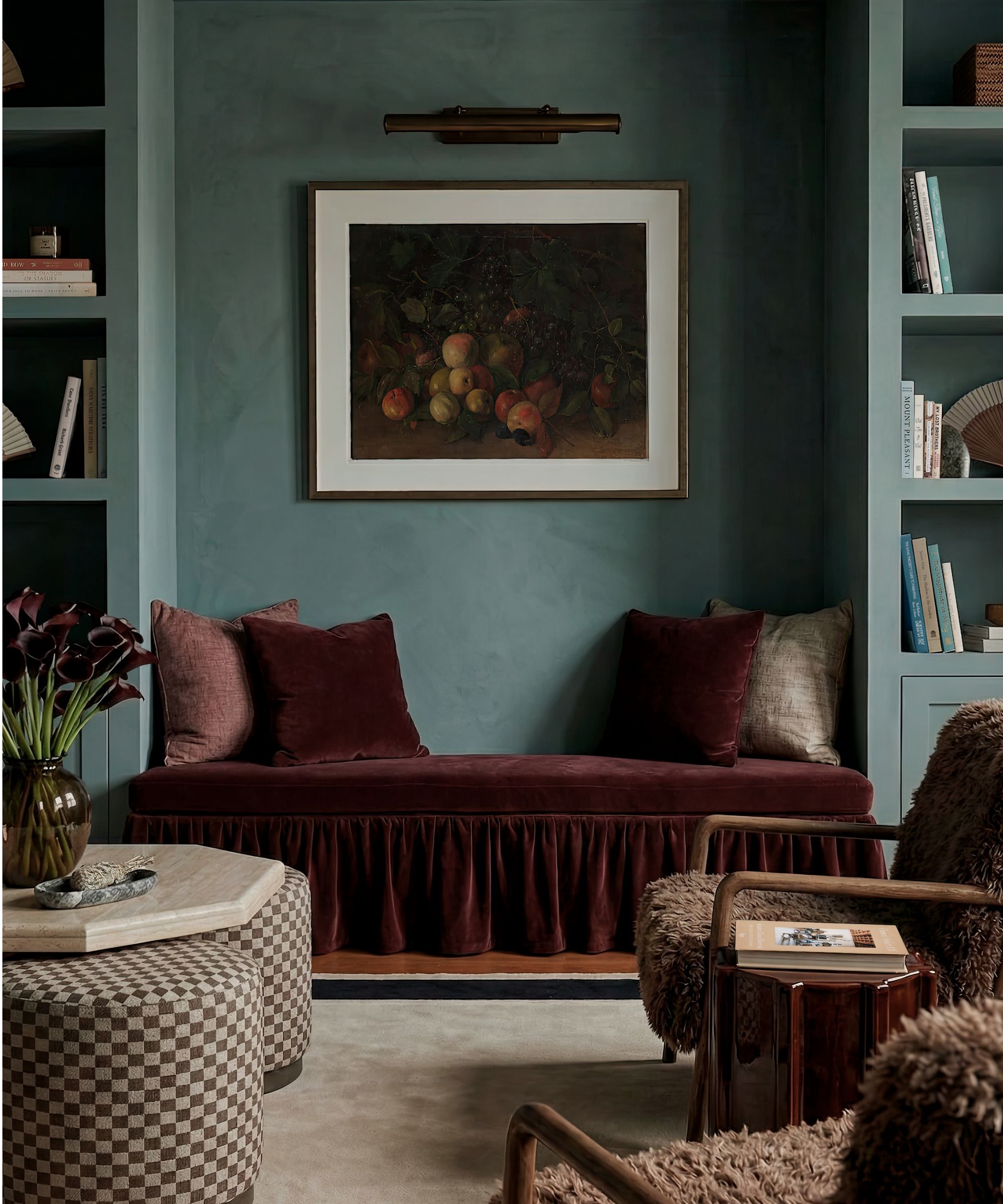 Living room with powder blue walls, built-in bench upholstered in red velvet with matching throw cushions, boucle armchairs, still life fruit painting and built-in bookcases
