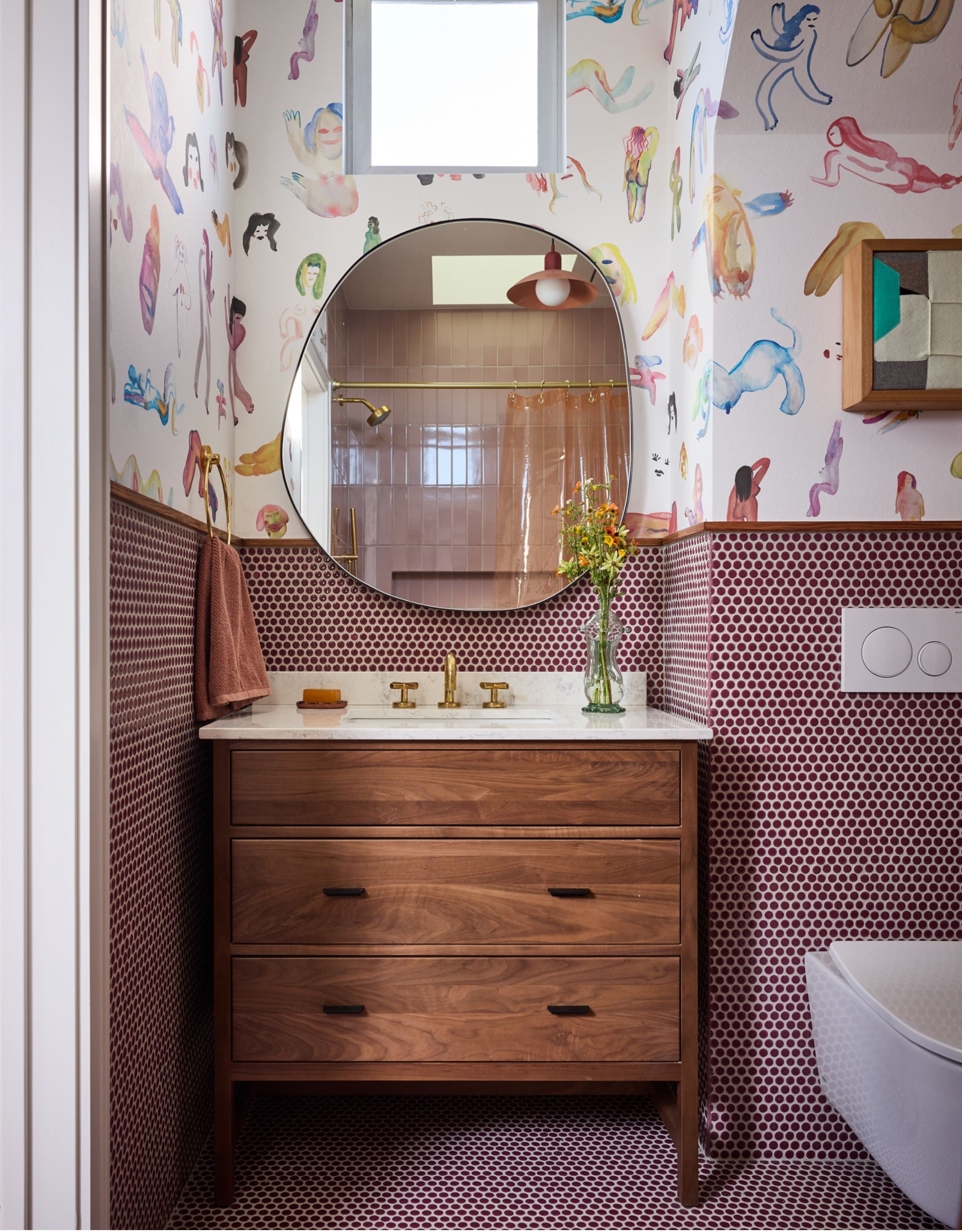 A playful pink guest bathroom with fun wallpaper, tiles, and a wood vanity with drawers