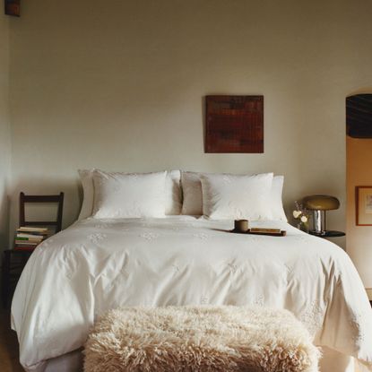 White bedroom with white bedding an a fluffy ottoman