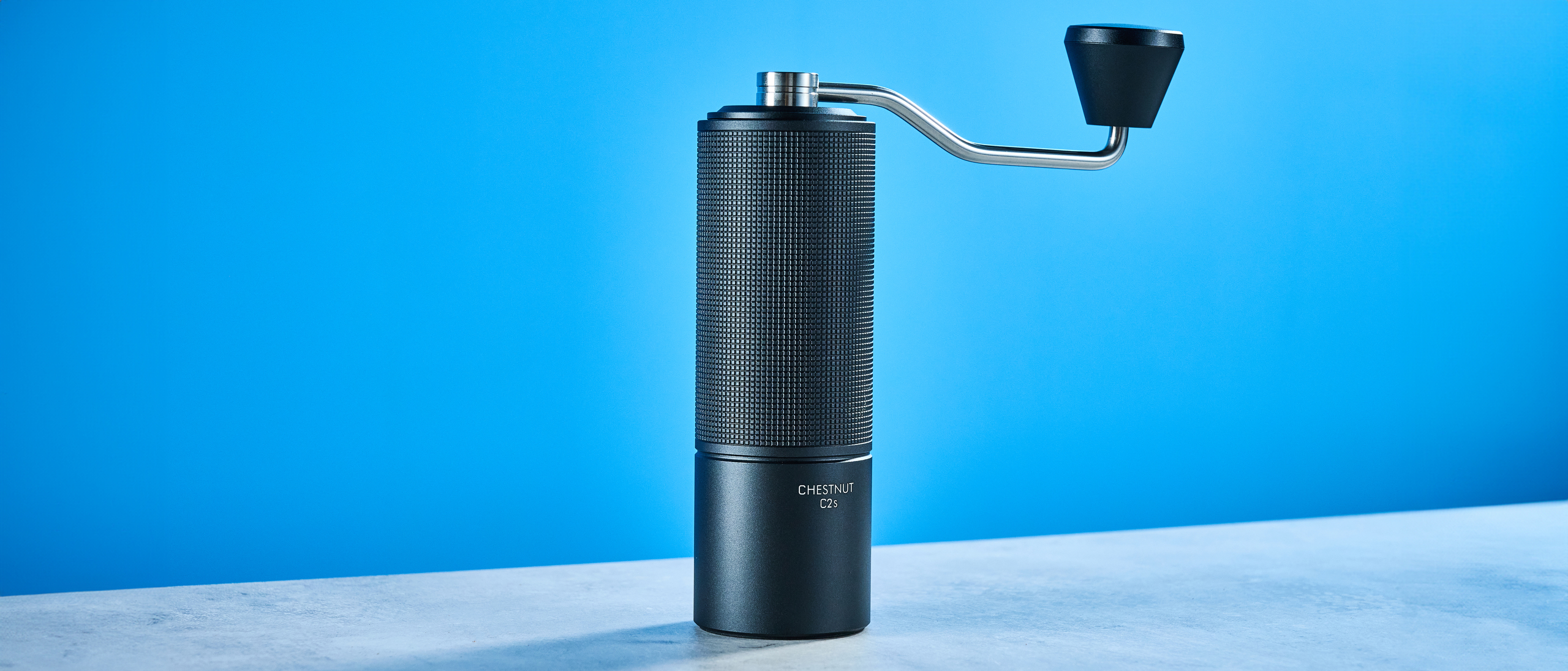 the timemore chestnut c2s coffee grinder in black showing its hand crank and catch chamber photographed against the blue tom's guide background