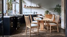 A kitchen diner with black kitchen cabinets and a large wooden dining table, surrounded by five matching wooden chairs.