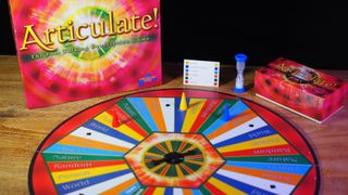 Articulate! box, board, tokens, and timer on a wooden table, against a black background