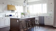 A 2015 kitchen with white cabinets, a wooden island, a brass range hood, and exposed appliances