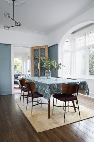 Dining room with dark wood floors, mid century dining chairs, blue paisley pattern tablecloth and blue panelled walls