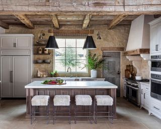 Large rustic kitchen with exposed beams and wooden features, stone walls, kitchen island with seating, low hanging pendants over island