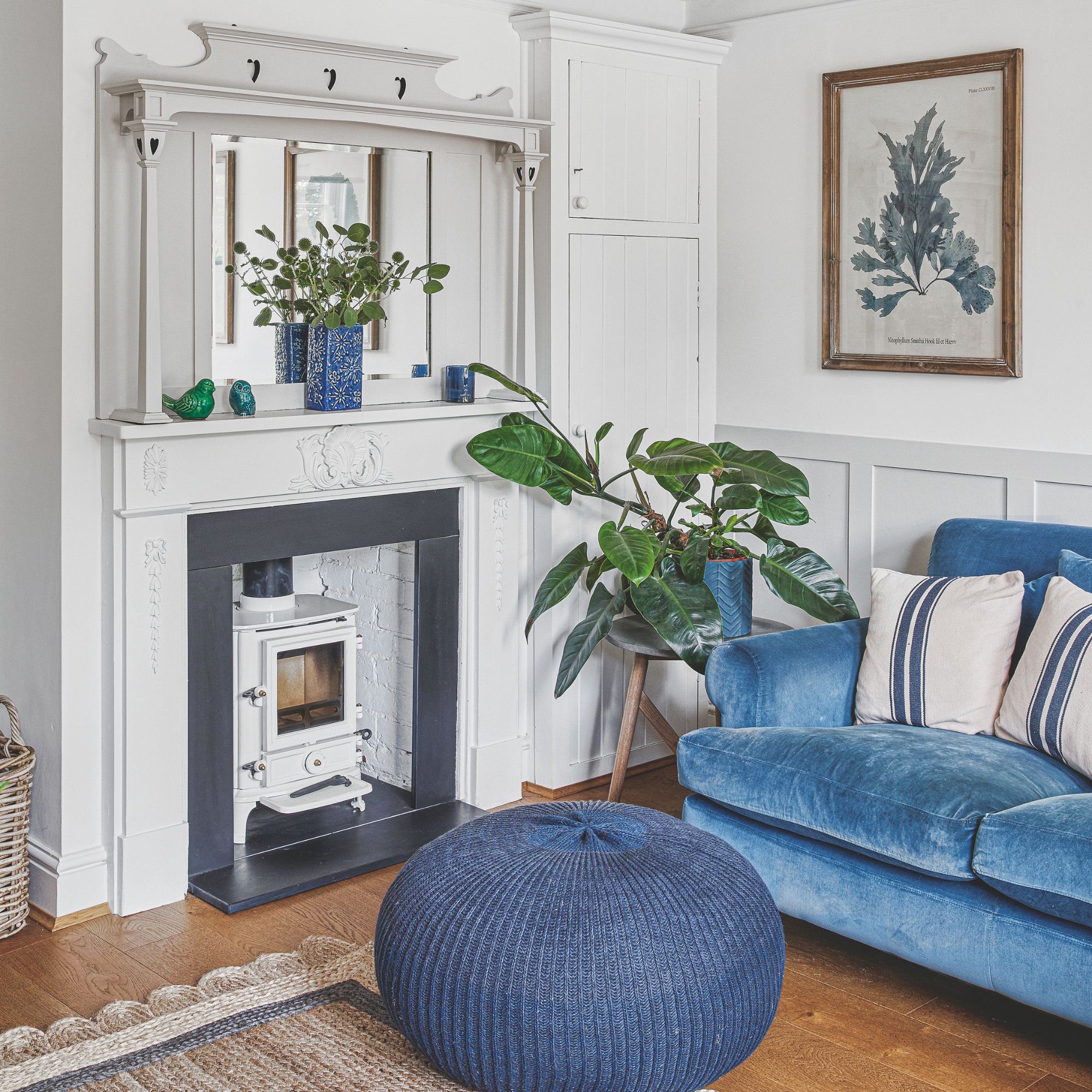 White painted living room with a blue sofa and matching pouffe in front of a white log burner