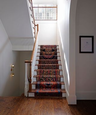 A white entryway with a staircase, patterned runner, and hardwood floors