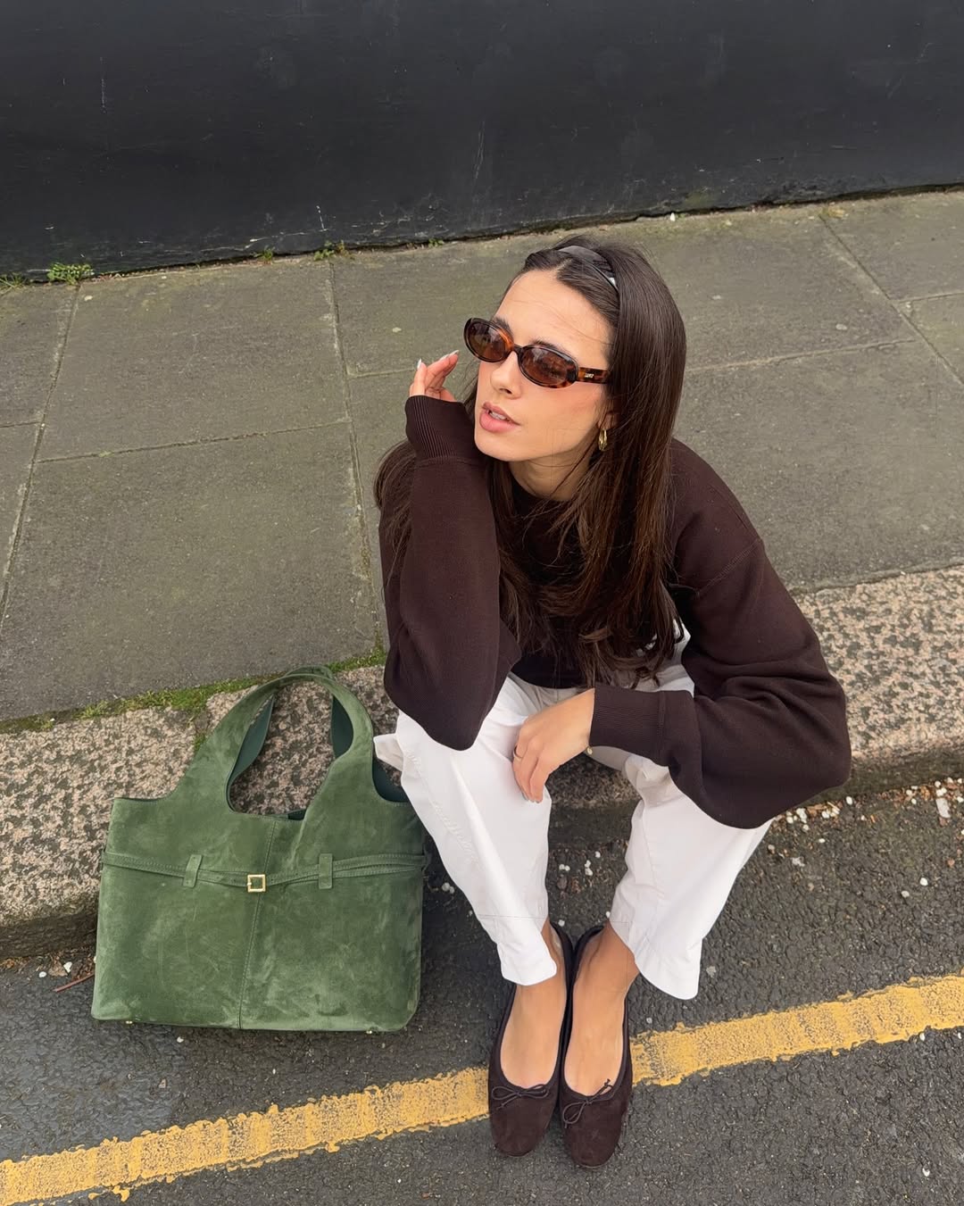 An image of a woman wearing a chocolate brown blouse and olive green handbag, one of the biggest 2026 spring color pairings.