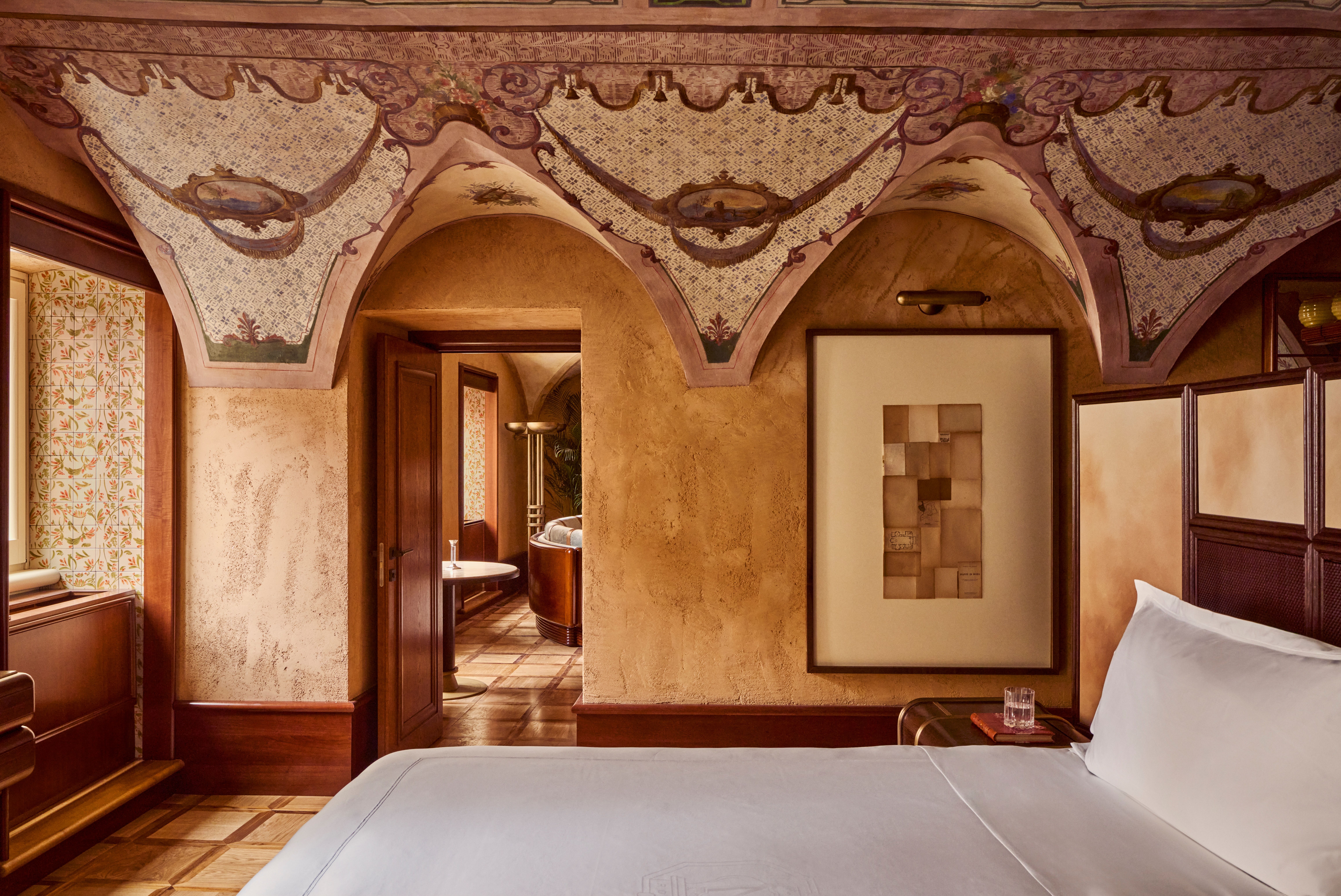 The interiors of a palatial hotel housed inside a 16th-century building with frescoed walls, textural arches, mesmerizing flooring, and plenty of wood oozes antique-inspired furniture and a golden atmosphere across sculptural furnishings, artworks, and plants.