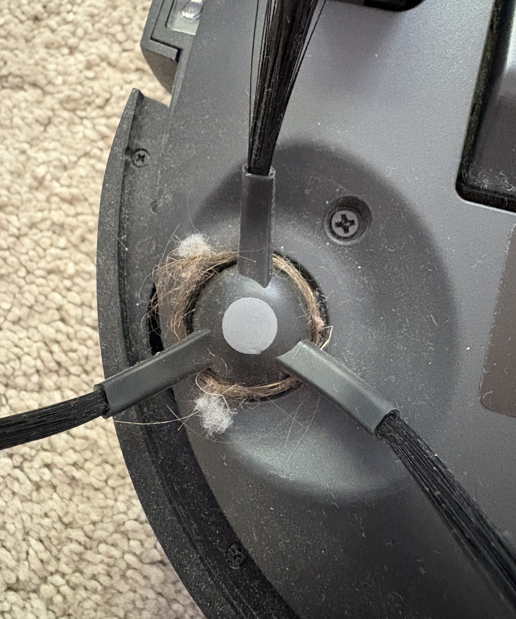 close up of brush on the bottom of a robot vacuum cleaner with hair wound around it