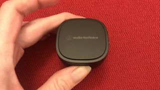 Audio-Technica ATH-SQ1TW case held in hand, on red background