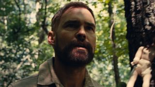 Seann William Scott standing in forest with doll nailed to tree in Dolly