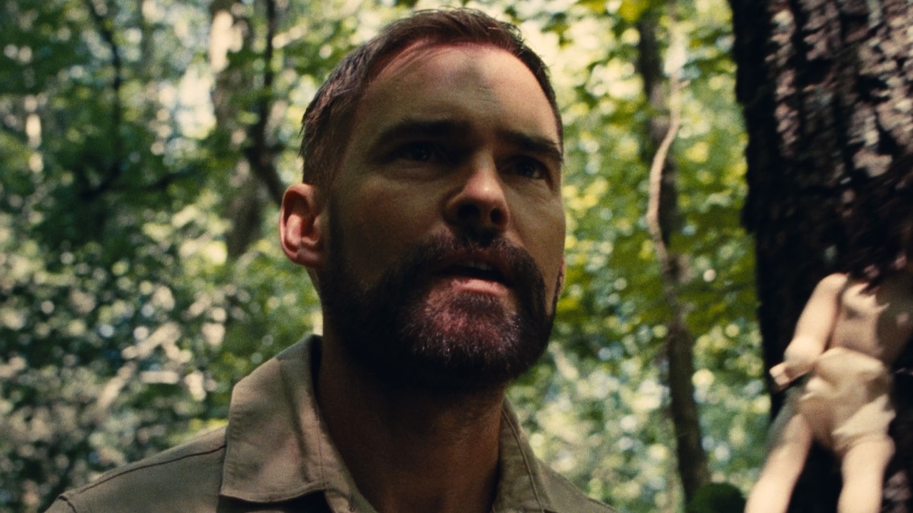 Seann William Scott standing in forest with doll nailed to tree in Dolly