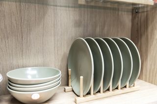 Various plates in a plate rack and bowls inside a cupboard.