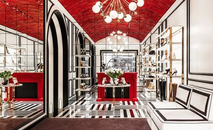 A room in white, black, and red tones. Two walls are covered in mirrors, and on the wall to the right, there is a black & white sitting area. On the table in the center shoes are displayed.