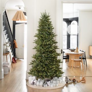 An open plan entryway and dining room with an undressed Christmas tree used as a partition