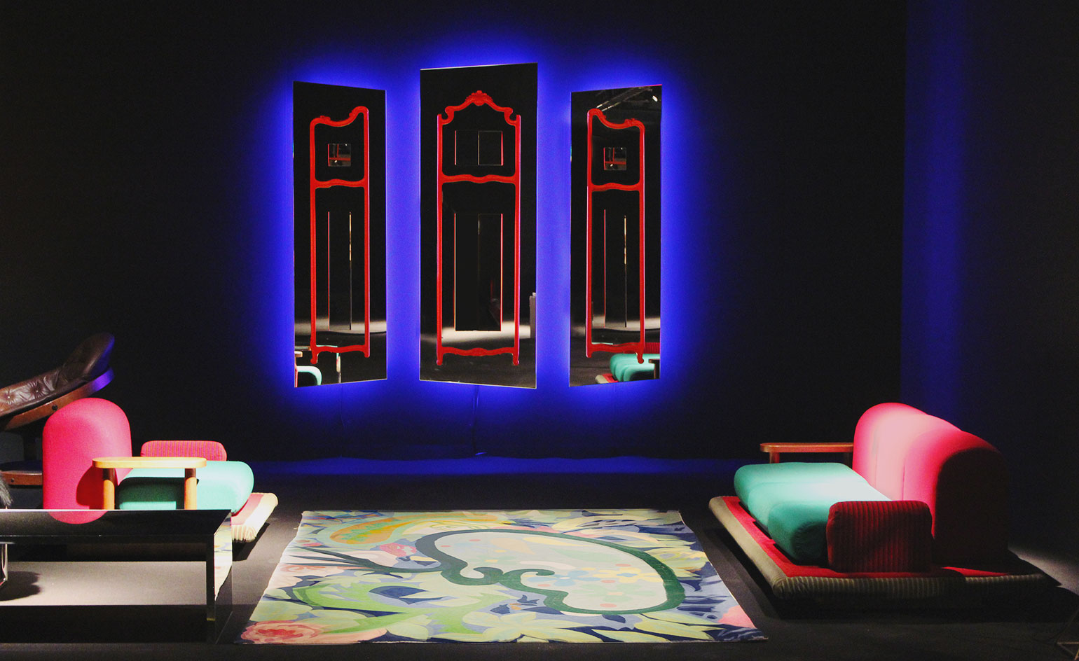 Milanese gallery Erastudio Apartment-Gallery had a blacked-out booth, where the dark mood enhanced the colourful nature of Ettore Sottsass' chair and sofa, and Nanda Vigo's mirrors and rug