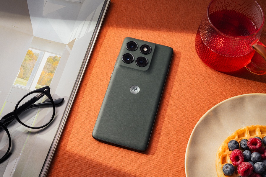 The Moto Edge 2025 lies on an orange table with a pair of glasses and breakfast nearby.