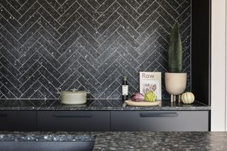 Herringbone tile backsplash with dark tile, dark countertop and dark cabinets in kitchen