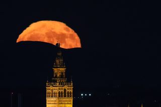 blood red full moon rising behind a mountain with a top of a cathedral in the foreground.