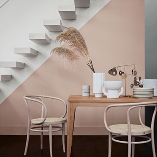 White floating stairs above a dining table in front of a pink wall