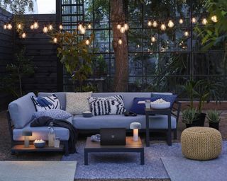 A patio area with a sofa, an outdoor festoon and table lights