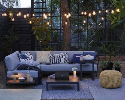 An example of how to install garden lighting showing an outdoor patio area with a sofa and bulb string lights above