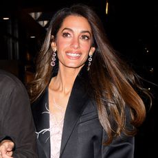 Amal Clooney smiles wearing crystal earrings and a black blazer