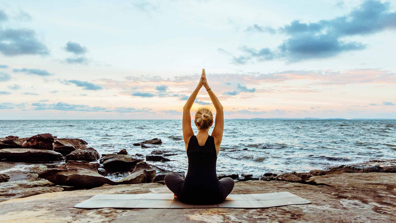 A woman does yoga at sunrise on a rocky beach.