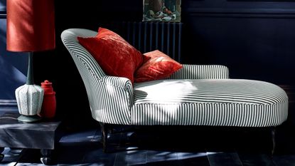 striped fainting sofa with red cushions next to table with a lamp with a red shade