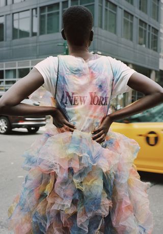 From The Colors of Sies Marjan. The back of a woman standing in the street wearing a colourful frilly dress.